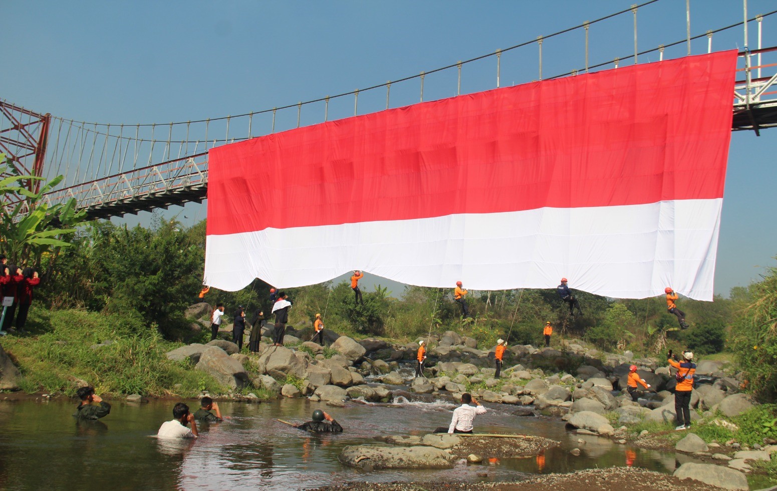 Kolaborasi SMK MIPHA, BPBD dan FPTI Bentangkan Bendera Merah Putih di Jembatan Gantung
